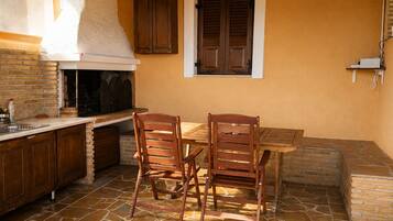 Un área de cocina al aire libre con suelo de piedra, mobiliario de madera y un horno de ladrillo.