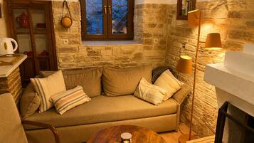 Una sala de estar acogedora con una pared de piedra, un mueble de madera, un sofá con cojines, una mesa redonda de madera y una lámpara de pie.