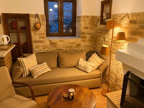 Una sala de estar acogedora con una pared de piedra, un mueble de madera, un sofá con cojines, una mesa redonda de madera y una lámpara de pie.