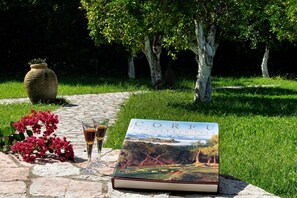 A book titled "The Garden Book" on a stone surface outdoors with a pathway, greenery, and a large vase.