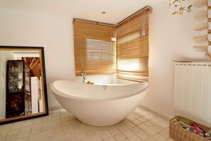 A modern bathroom with a freestanding bathtub, wooden blinds, a mirror, and a radiator.