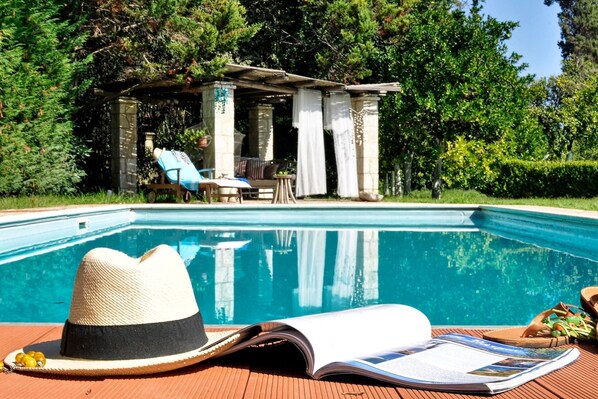 Ein Poolbereich mit Liegestuhl, Hut und Zeitschrift auf einer Holzterrasse.