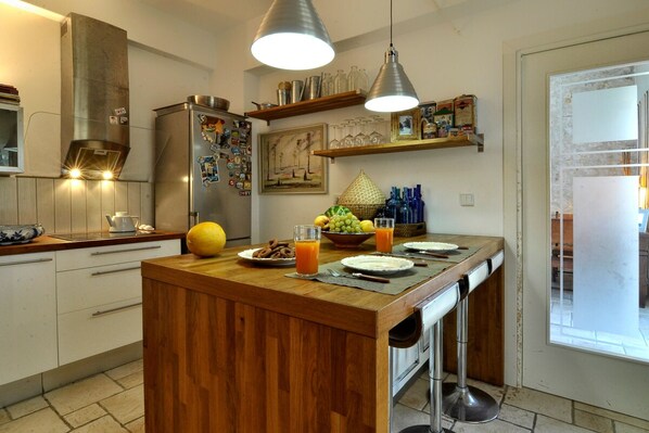 Una cocina con isla de madera, electrodomésticos de acero inoxidable e iluminación colgante.