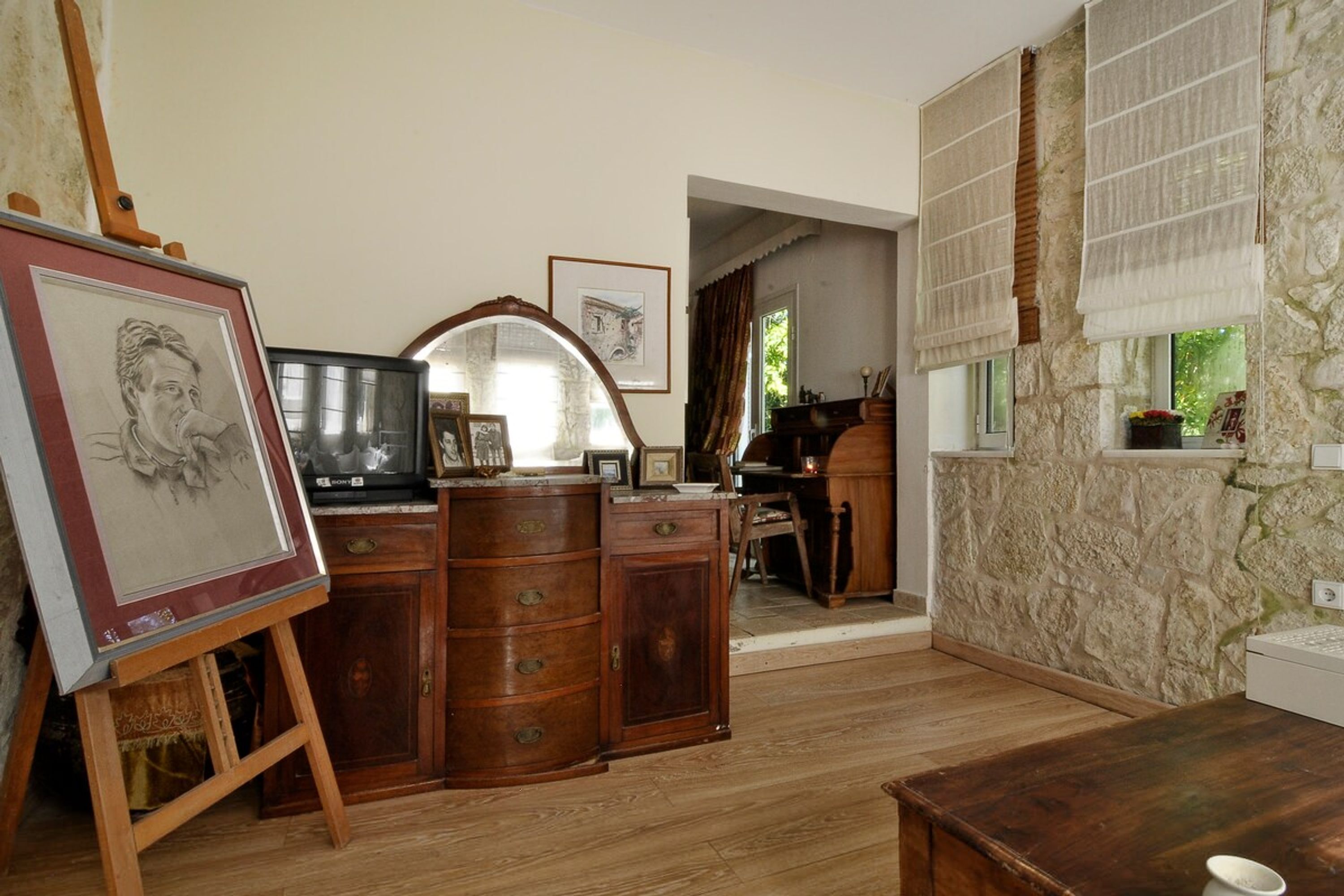 Una habitación con un escritorio de madera, un cuadro en caballete, un espejo y una pared de piedra.