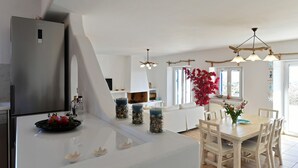 A modern kitchen with a stainless steel refrigerator, a dining area with a wooden table and chairs, and a large window with a view of the outdoors. - Dreamcatcher Sea View Mini Pool Paros (Paros)