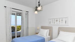 A bedroom with two beds, a window with curtains, a wall-mounted light fixture, and a framed picture. - Dreamcatcher Sea View Mini Pool Paros (Paros)