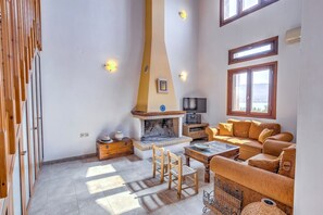 A cozy living room with a fireplace, wooden furniture, and a sofa with cushions. - Sea Front Stone Villa Near Monemvasia (Monemvasia)