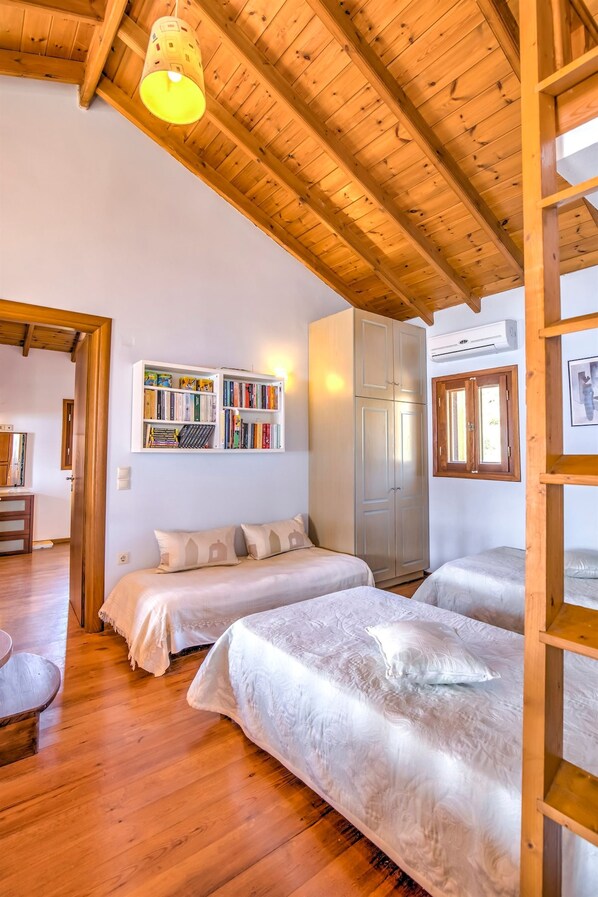 A cozy room with two beds, wooden ceiling beams, a bookshelf, and a wardrobe. - Sea Front Stone Villa Near Monemvasia (Monemvasia)