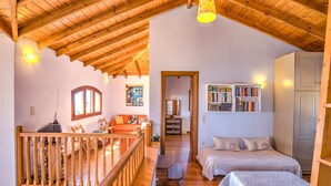 A cozy room with a wooden ceiling, a balcony, a bed, a bookshelf, and a desk with a lamp.