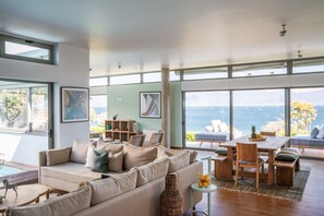 Un salón amplio con un gran ventanal con vistas panorámicas, una zona de estar acogedora y una mesa de comedor con sillas.
