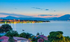 Un pueblo a orillas del lago al anochecer, con edificios iluminados, un lago tranquilo y montañas al fondo.