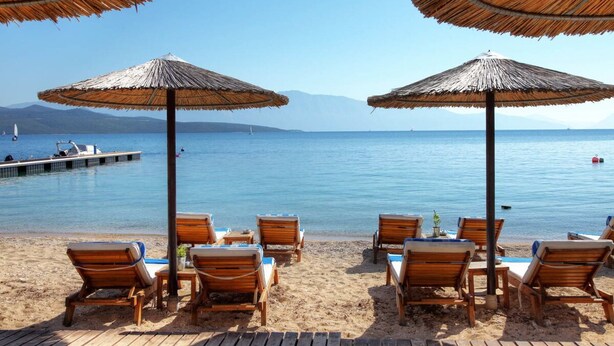 Une plage avec des chaises longues en bois et des parasols en chaume, une jetée et une mer calme.