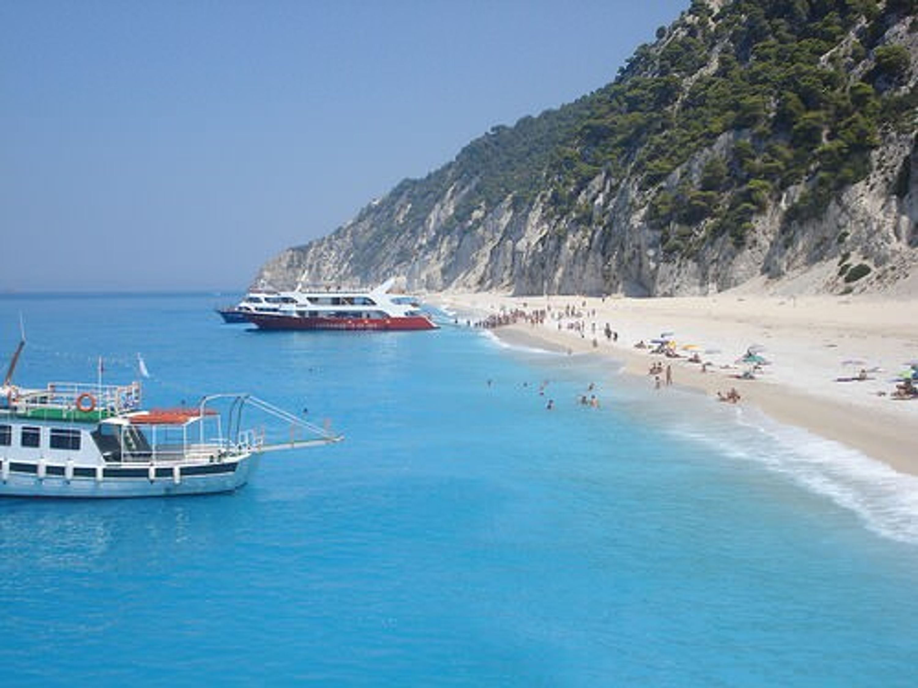 A coastal scene with a boat docked near a sandy beach, surrounded by rocky cliffs.