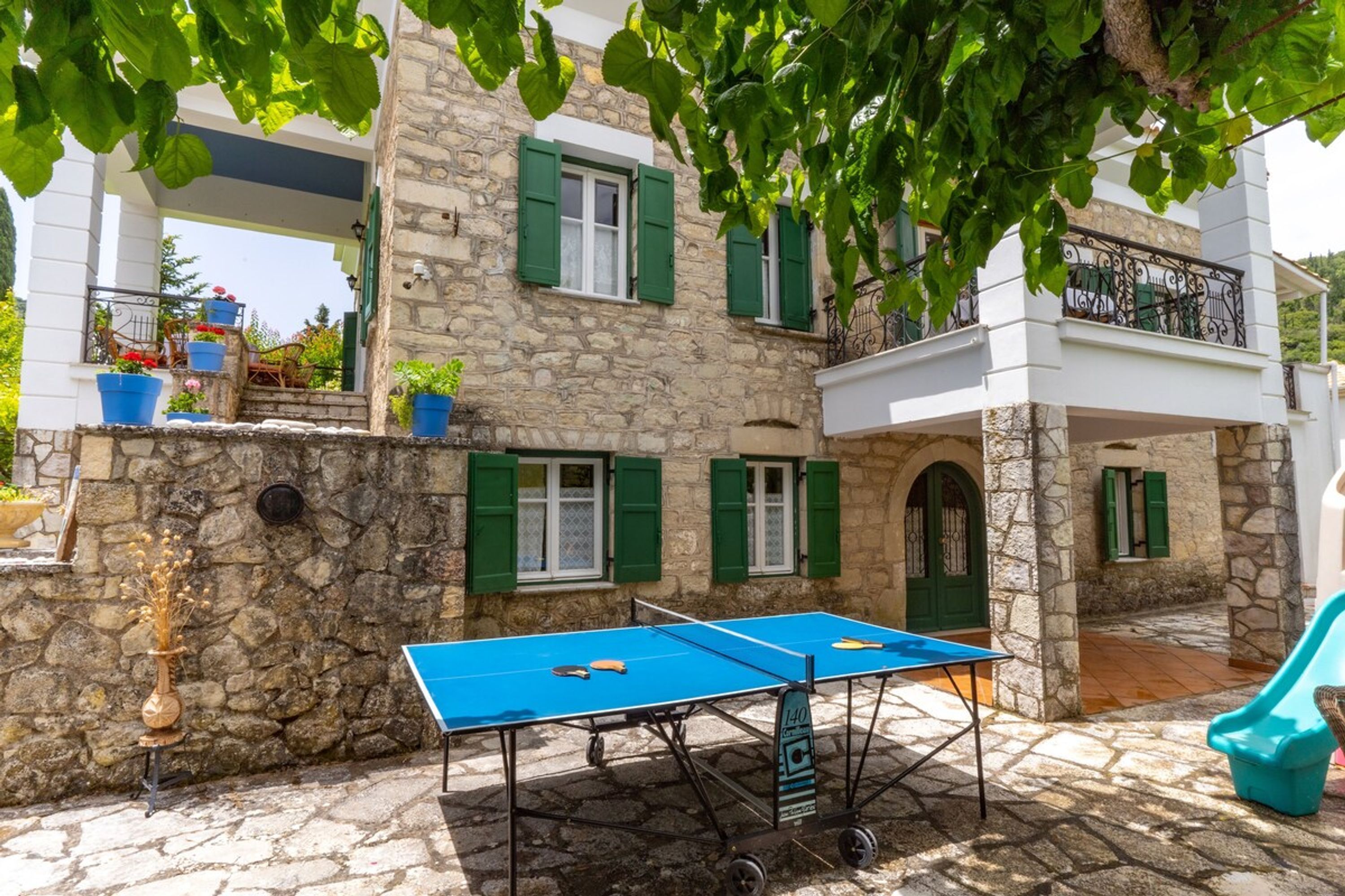 Ein Steinhaus mit grünen Fensterläden, einem Tischtennis-Tisch und Außenbestuhlung.
