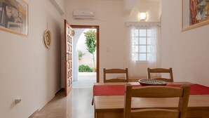 A dining area with a wooden table and chairs, a red tablecloth, and a window with white curtains. - Naousa Central House Paros (Paros)