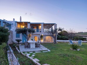 Une maison moderne avec une façade en pierre, un patio doté de mobilier d’extérieur et une vue sur le paysage environnant.