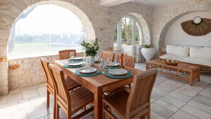 A dining area with a stone wall, wooden furniture, and a view through an arched window. - Sunrise Serenity Near Ambelas Beach (Paros)