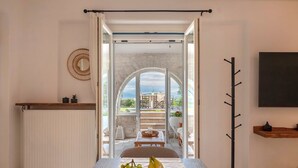 A dining area with a table set for two, a fruit bowl, and a view of an outdoor patio with a table and chairs. - Sunrise Serenity Near Ambelas Beach (Paros)