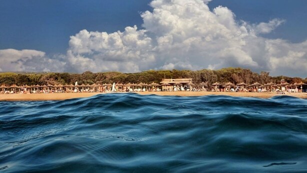 A beach with umbrellas and people, a building in the background, and a cloudy sky. - Agrilis Cottage Near the Beach (Trifylia)