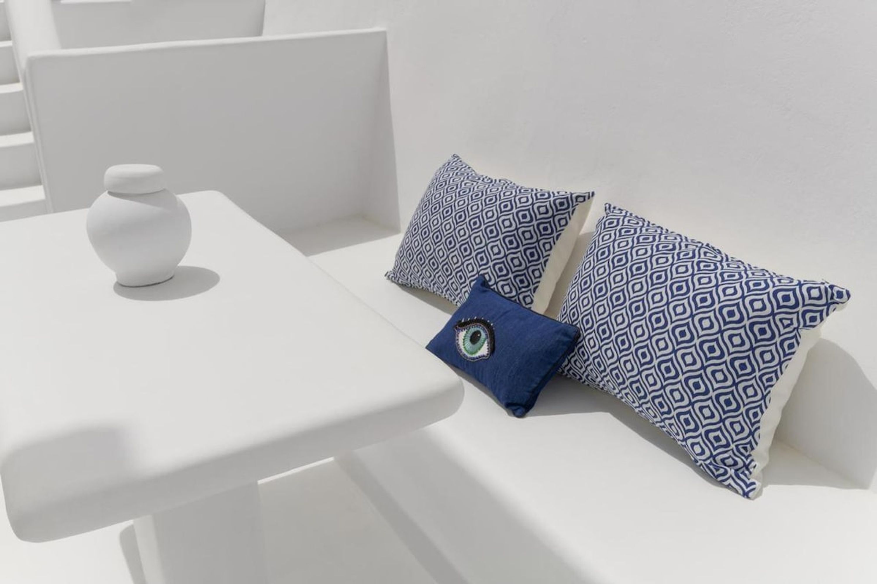 Een witte bank met gekleurde kussens en een kleine witte vaas op een witte tafel.