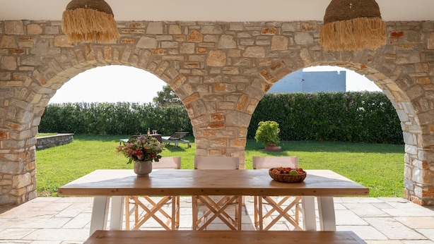 An outdoor patio with a stone archway, a wooden table, and hanging light fixtures. - Villa Franca Ideal for Wedding Parties (Paros)