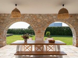 Un patio exterior con un arco de piedra, una mesa de madera y lámparas colgantes.