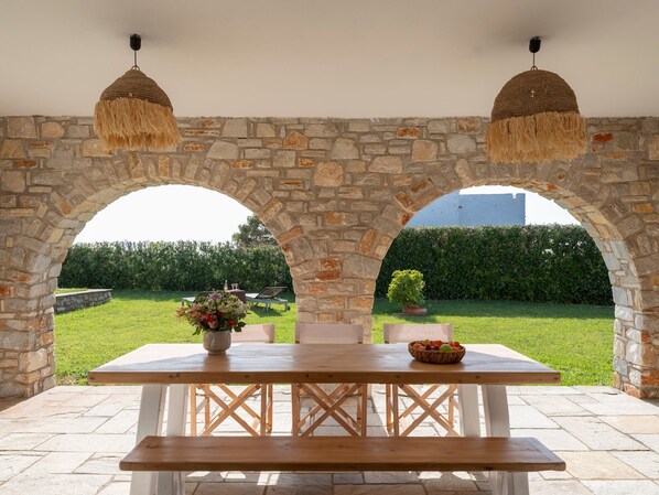 Un patio exterior con un arco de piedra, una mesa de madera y lámparas colgantes.
