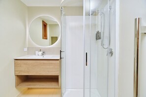 A modern bathroom with a glass-enclosed shower, a wooden vanity, and a round mirror.