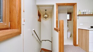Un couloir étroit avec une porte en bois, une main courante et un luminaire au plafond.
