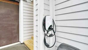 Une borne de recharge pour véhicules électriques fixée à la façade extérieure d’une maison blanche.