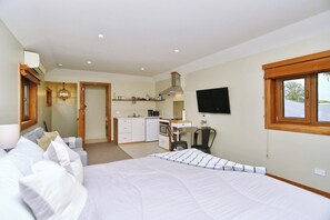 A bedroom with a large bed, a kitchenette with a TV, and a window with a view.