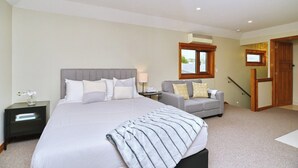 Une chambre avec un grand lit, un canapé gris, une petite table avec une lampe et une fenêtre donnant sur un beau paysage.