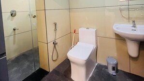 A modern bathroom with a glass shower enclosure, a toilet, a sink, and a small trash bin. - Spexxa Residency (Kozhikode)