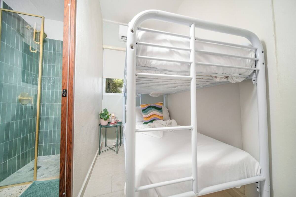Uma cama beliche em quarto com área de chuveiro e uma pequena mesa com uma planta.