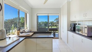 A modern kitchen with white cabinets, a large window, and a ceiling fan.