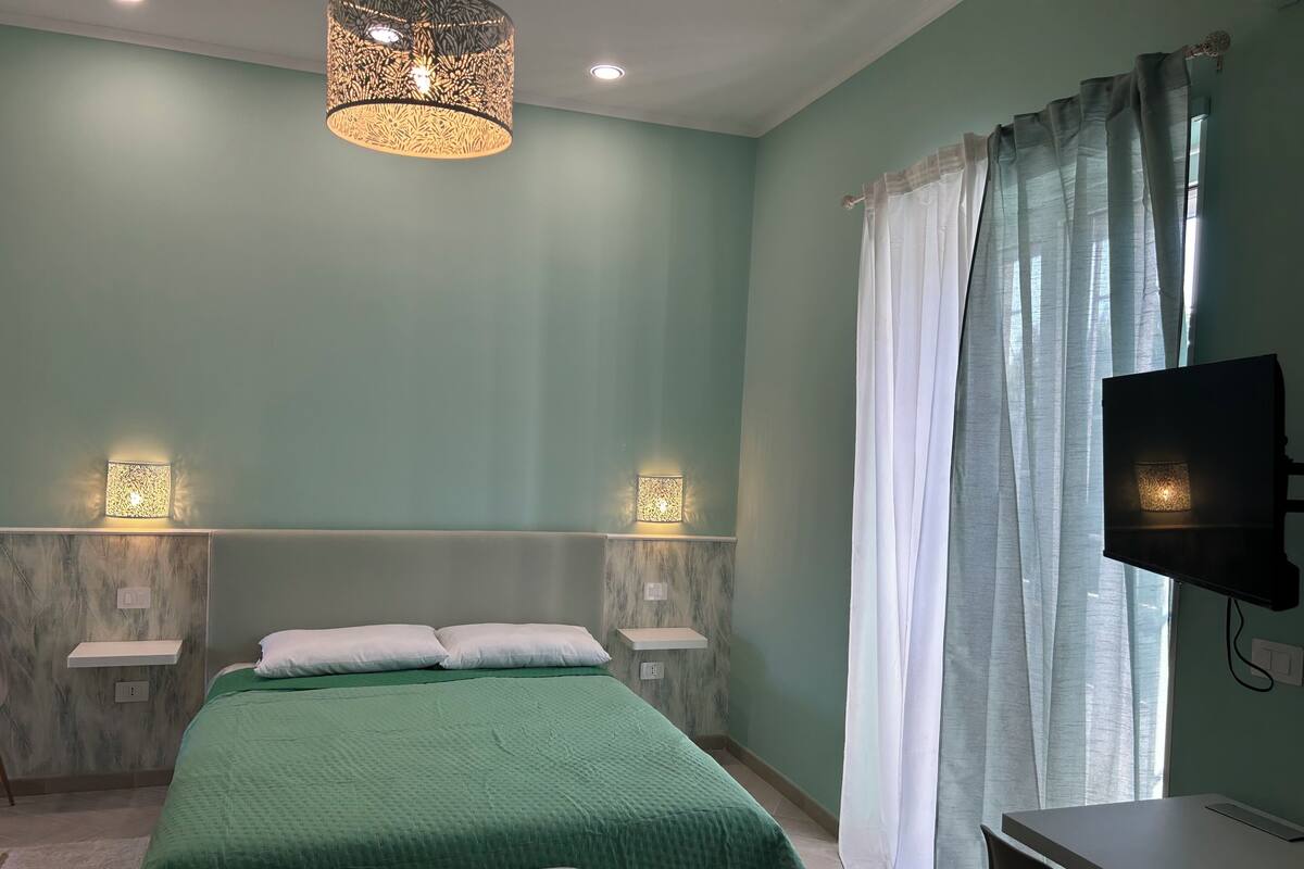 A bedroom with a bed, bedside tables, a TV, and a ceiling light fixture.