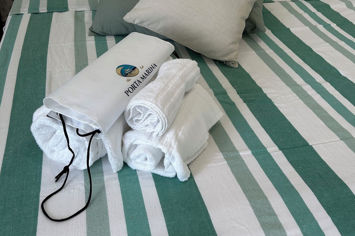 A neatly made bed with striped bedding, pillows, and rolled towels with a tag.