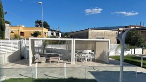 Un espacio de estar techado al aire libre con una mesa y sillas, rodeado por una cerca blanca.