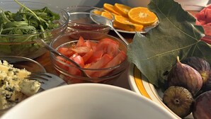 Una mesa con diversos alimentos, entre ellos una ensalada, tomates, higos y un bol de queso.