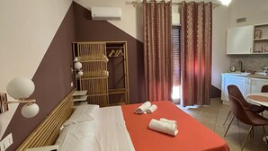 A hotel room with a bed, bedside table, lamp, air conditioning unit, wardrobe, and a kitchenette area. - B&B Elegance (Villa San Giovanni)