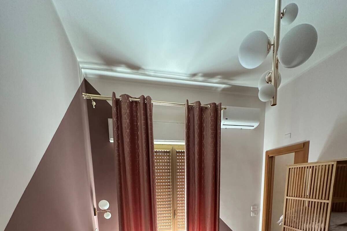 Une chambre d’hôtel comprenant un lit, une armoire en bois, un miroir, une fenêtre avec des rideaux et un luminaire au plafond.