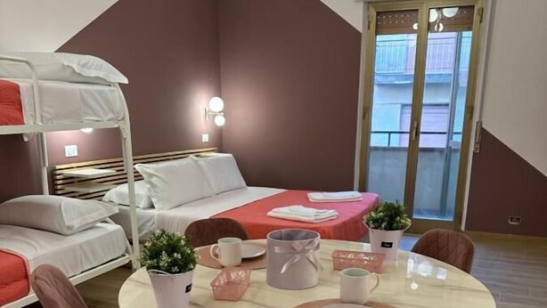 A modern room with a bunk bed, a round dining table with chairs, and a small kitchen area. - B&B Elegance (Villa San Giovanni)