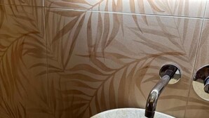 A bathroom with a marble sink, a mirror above it, and patterned wall tiles. - B&B Elegance (Villa San Giovanni)