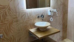 A bathroom with a leaf-patterned wall, a wooden vanity with a sink, and a mirror above the mirror. - B&B Elegance (Villa San Giovanni)