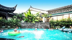 A swimming pool with a traditional building in the background, surrounded by lush greenery. - Meshee Sezen Hotel Suzhou (Suzhou)
