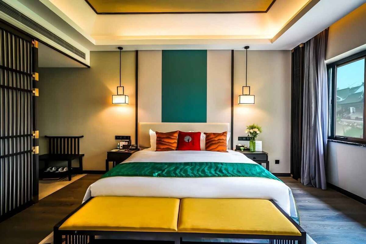 Ein modernes Hotelzimmer mit einem großen Bett, zwei Nachttischen, einer Bank und Blick durch ein Fenster nach draußen.