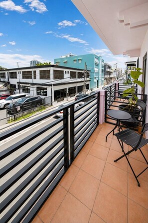 A balcony with a view of a street, a parking area, and a building with a blue facade. - Room 12: Sunlit Balcony Stay Near Calle Cerra (San Juan)