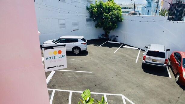 Un estacionamiento de hotel con espacios delimitados, un cartel que dice 'HOTEL LUZ' y plantas en macetas.