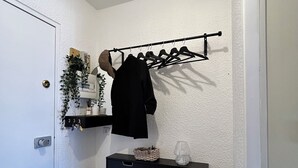 Un pasillo con un aparador negro, un perchero con ropa, una planta en maceta y una puerta.