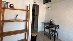 Una cocina moderna con estante de madera, una mesa de comedor con sillas y un pequeño cubo de basura.